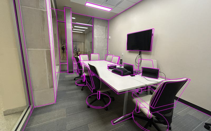 A conference room photographed on a phone, with the 3D model's edges drawn over it in magenta